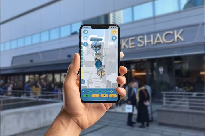 Hand holding smartphone displaying GPS walking tour map app in front of Shake Shack in Yokohama