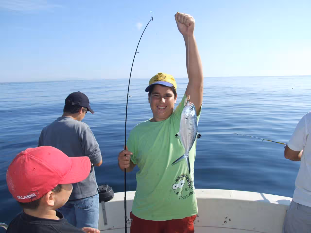 Young angler proudly displays his catch on a sport fishing boat trip, surrounded by calm ocean waters and clear skies.