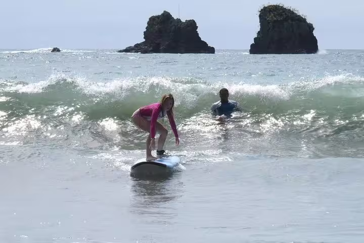 Young surfer riding a wave with an instructor nearby at scenic Manuel Antonio beach.