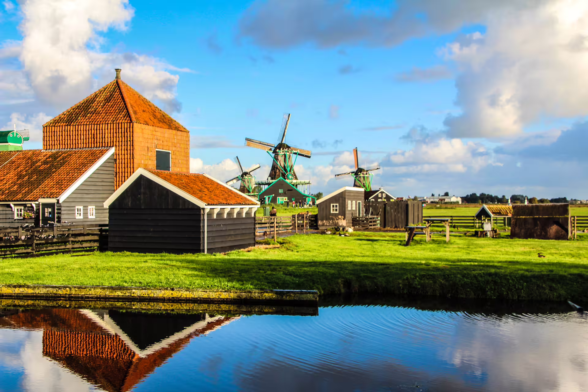 Scenic view of traditional windmills and historic buildings reflected in a canal at Zaanse Schans, Netherlands.