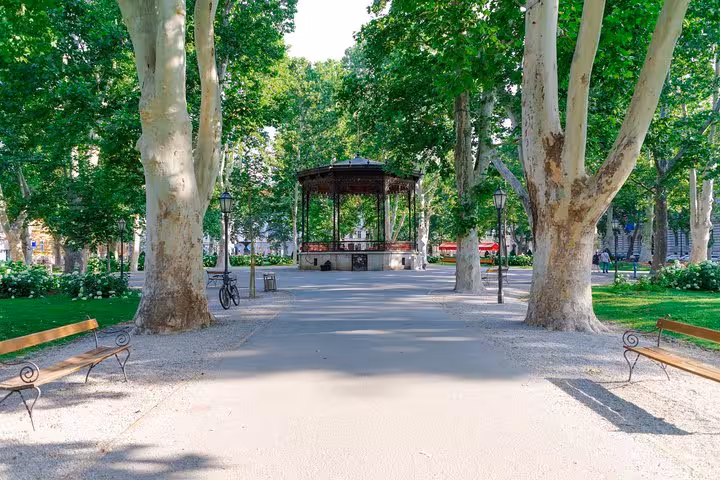 Zagreb BIG Tour stop at Zrinjevac Park, shady tree-lined promenade with pavilion and benches in Croatia
