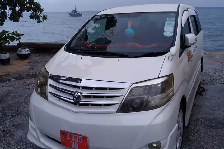 White shuttle vehicle parked near the beach, ready for Zanzibar airport transfers and island tours.