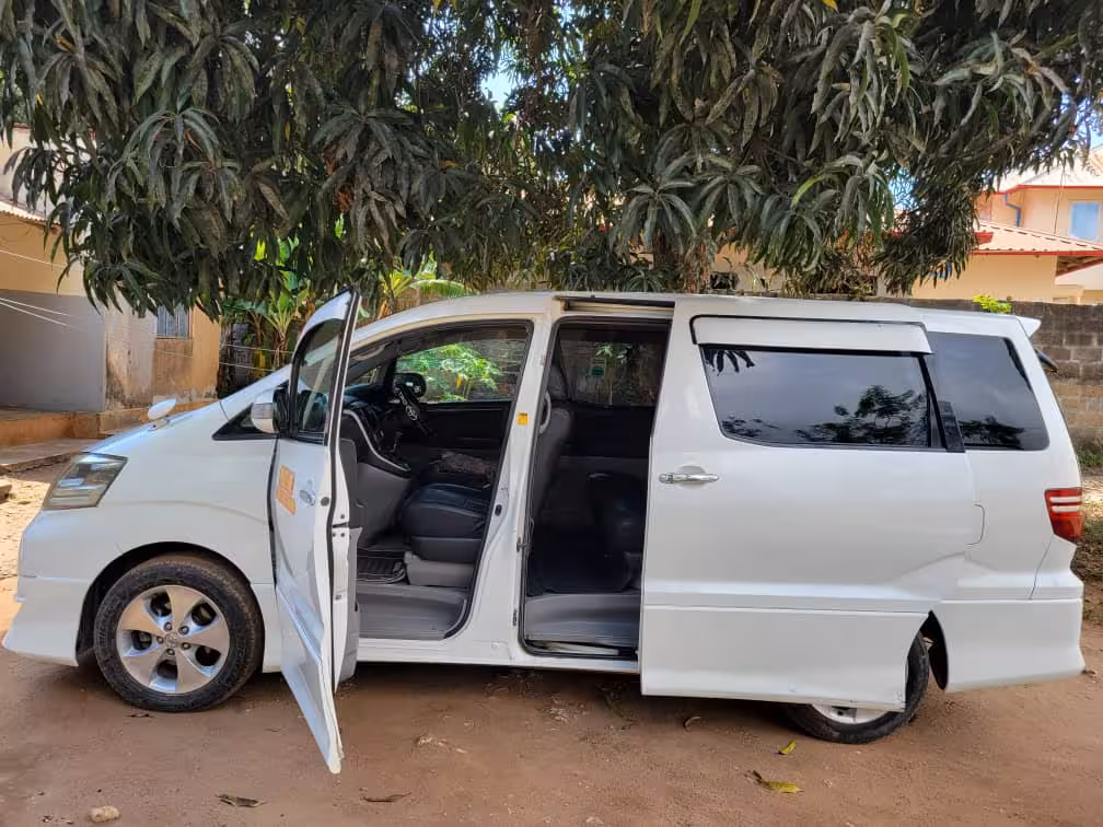 White airport taxi van parked in a shaded area, ready for private transfers to hotels in Pongwe, Zanzibar.