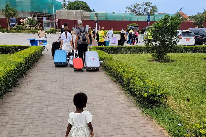 Travelers with luggage walking towards transport at Zanzibar Airport for East Coast hotel transfer.