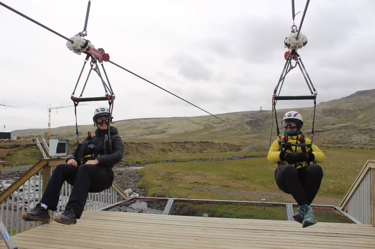 Two adventurers on a thrilling zipline ride over scenic landscape, wearing helmets and harnesses, perfect for outdoor excitement.