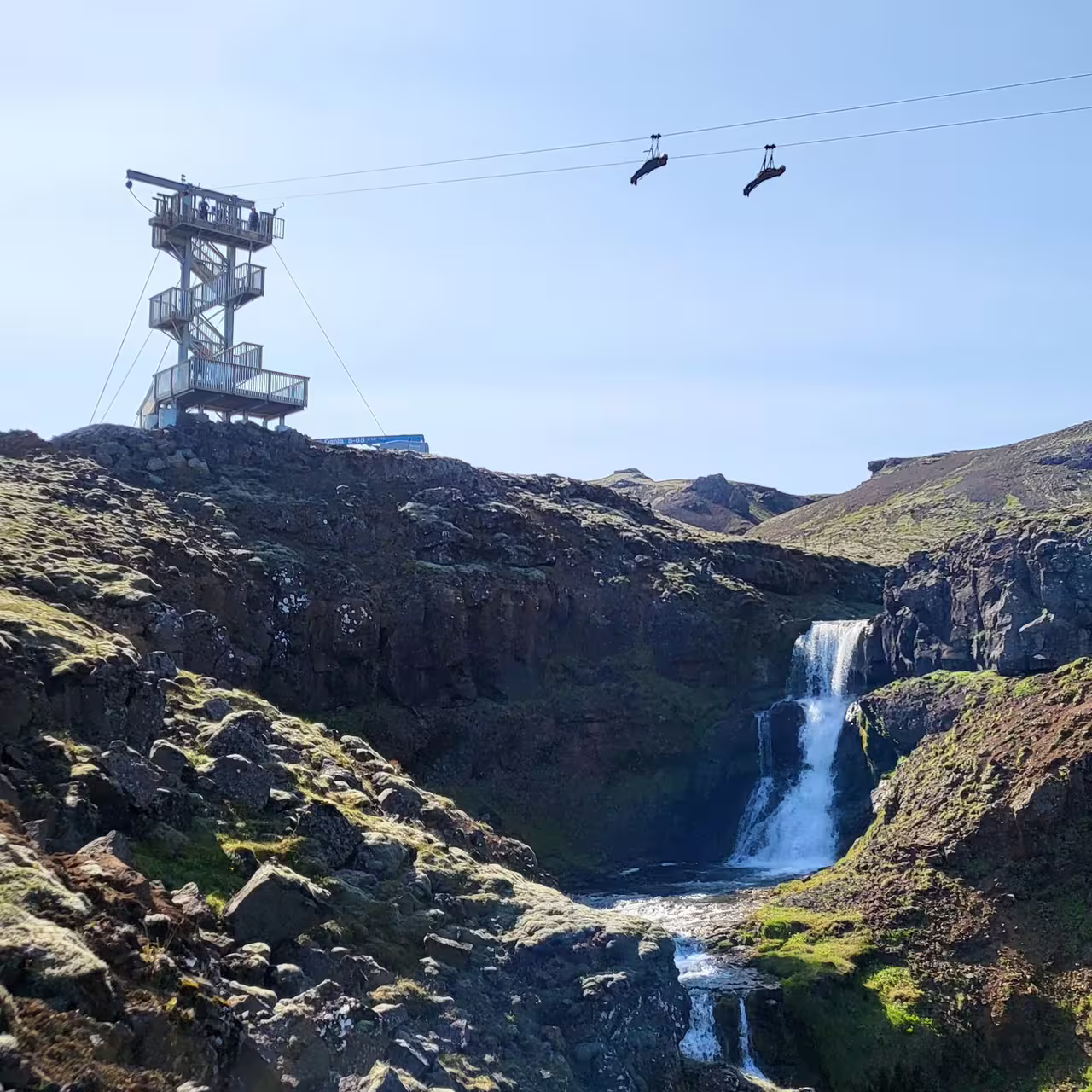 Thrilling zipline adventure over scenic waterfall and rugged landscape with observation tower, perfect for adrenaline seekers.