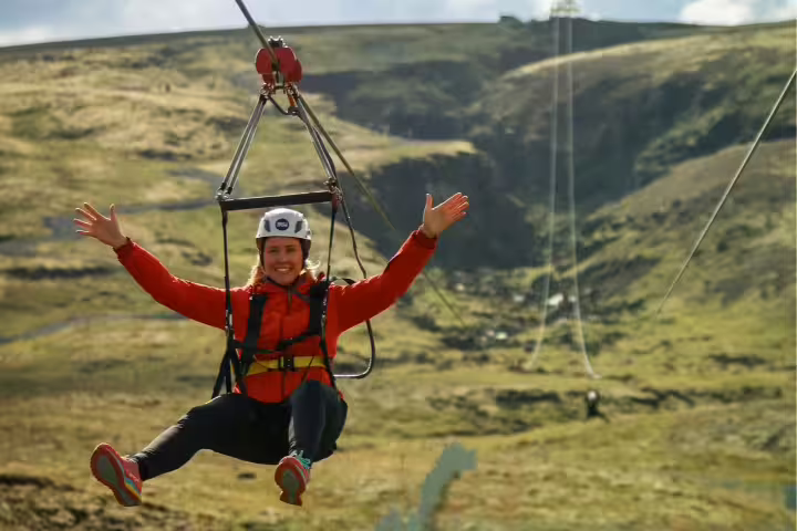 Person enjoying an exhilarating zipline ride over scenic landscape, arms outstretched in excitement, under a clear sky.