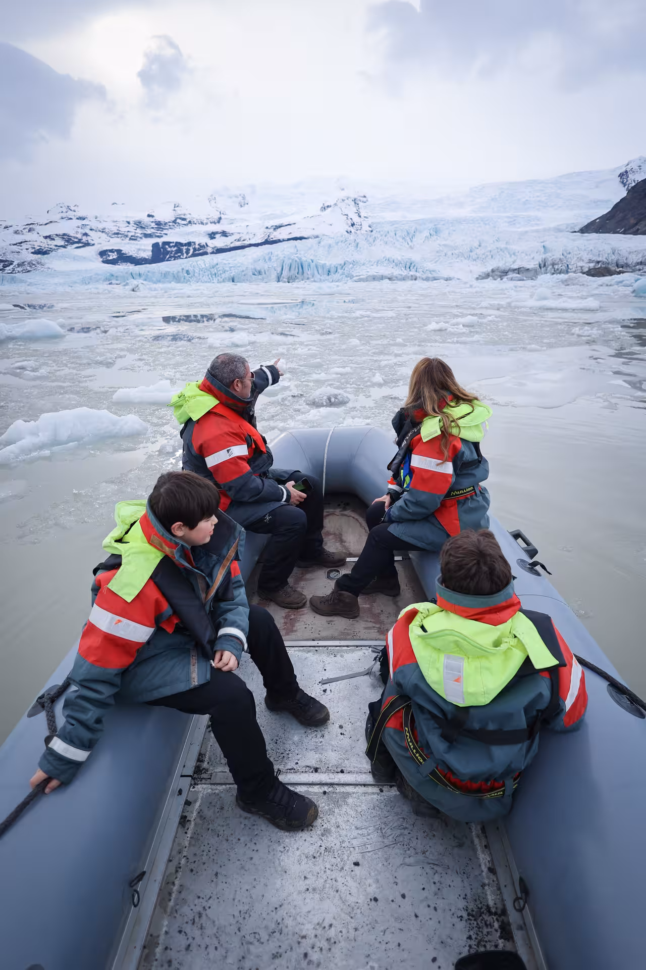 Guide pointing out glaciers to tourists on a zodiac boat tour amid icebergs in Iceland lagoon