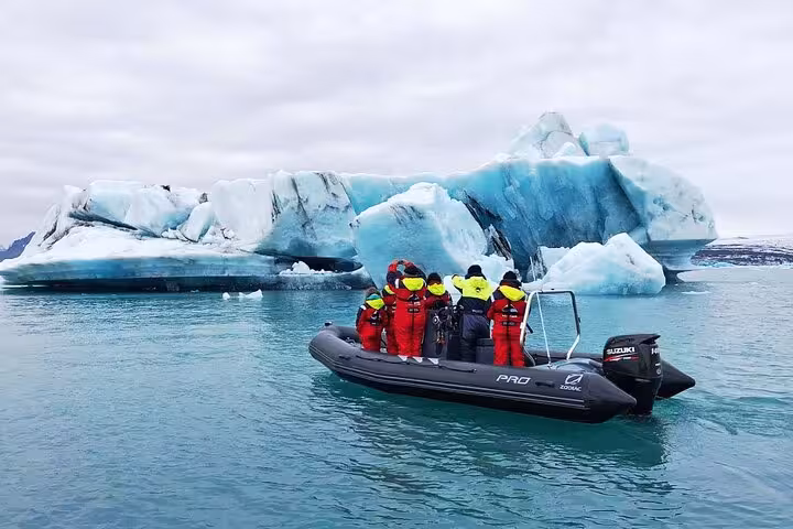Group in red suits on inflatable boat near blue icebergs at Jokulsarlon glacier lagoon Iceland