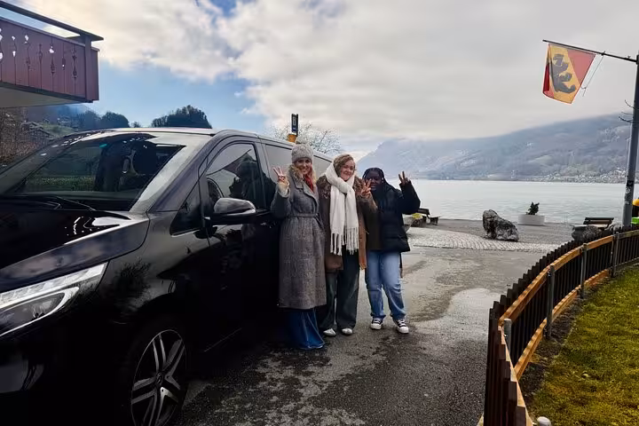 Happy travelers beside private minivan, scenic Swiss lake stop on Zurich Airport transfer with chauffeur