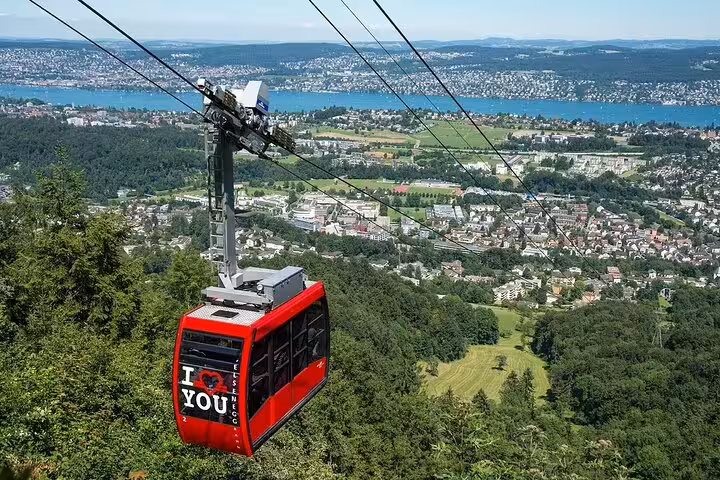 Scenic cable car ride over lush forests and cityscape of Zurich, offering panoramic views and a thrilling experience.