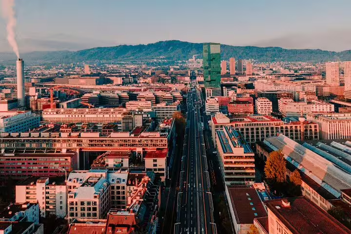 Aerial view of Zurich cityscape with wide boulevard, urban buildings, and green hills in the background