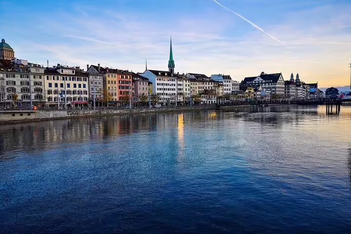 Zurich old town waterfront along the Limmat River with colorful historic buildings and church spire at dusk