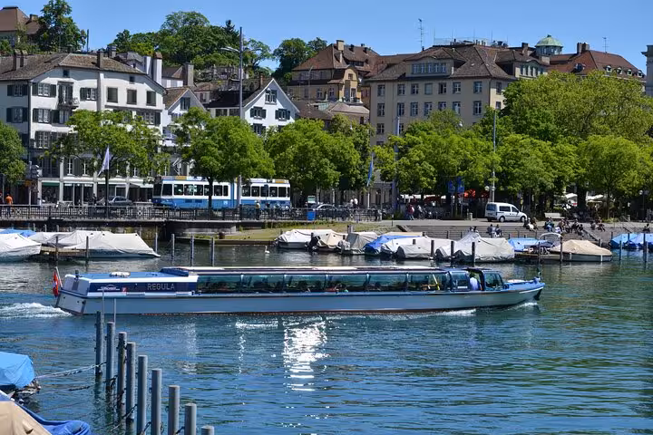 Scenic boat cruising on Lake Zurich with lush green trees and historic buildings in the background.