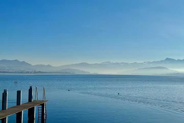 Calm lake with wooden dock, mountains in background, near Zurich on a clear blue day