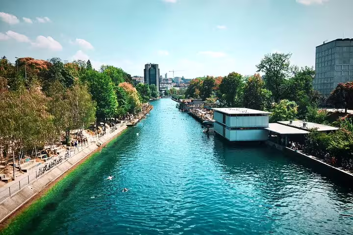 Turquoise Limmat River canal with tree-lined promenade and floating bathhouse in Zurich, Switzerland