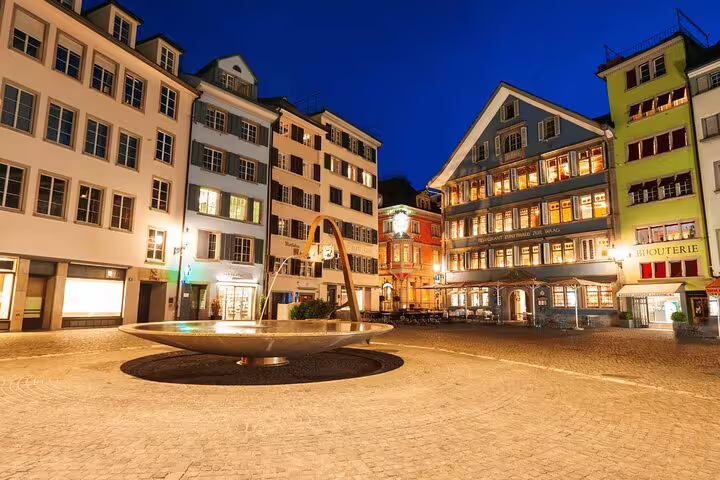 Charming evening scene in Zurich's old town with illuminated historic buildings and a central fountain.