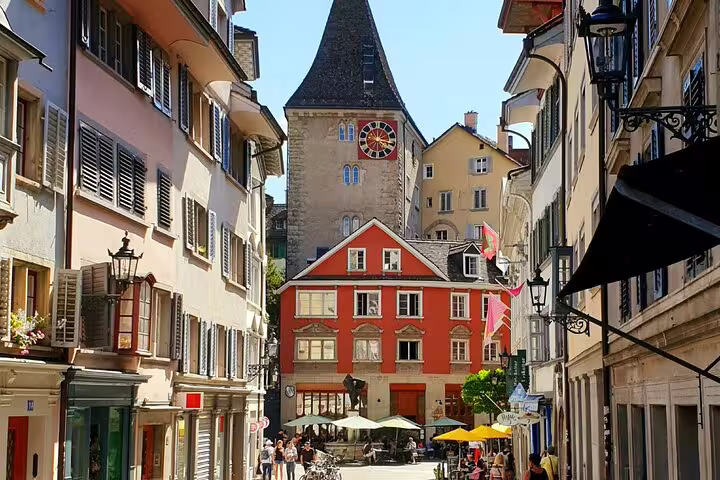 Narrow historic street in Zurich old town with red building and medieval clock tower