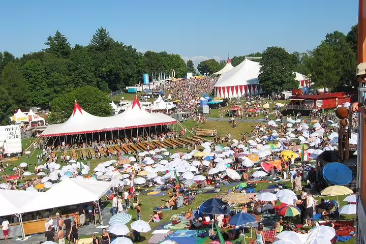 Aerial view of crowded outdoor festival with white tents, umbrellas, and visitors on green lawn in Zurich