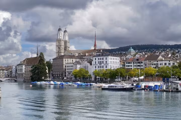 Scenic Zurich cityscape with historic churches and boats along the Limmat River, perfect for transportation adventure tours.