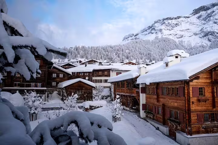 Snow-covered Swiss alpine village with wooden chalets and forested mountain backdrop in winter