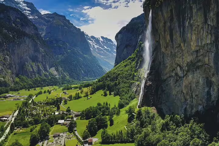 Lauterbrunnen valley with Staubbach waterfall cascading down cliffs, green meadows and Swiss Alpine village below