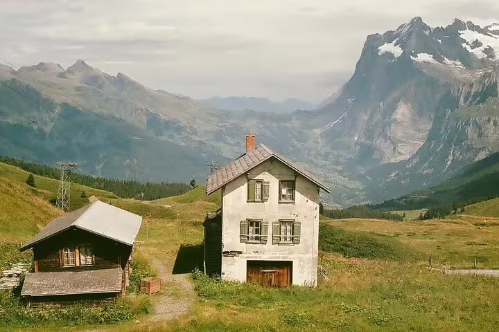 Alpine farmhouse and wooden chalet on green hillside with snow-capped Swiss mountains in background