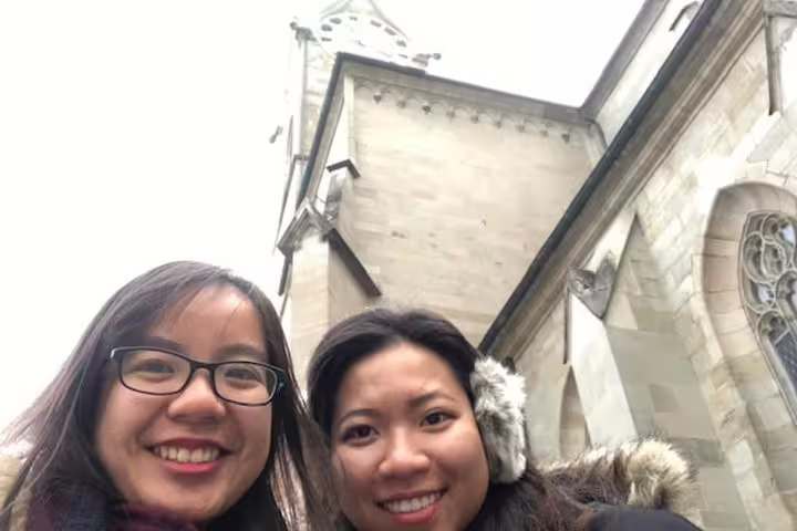 Two smiling women taking a selfie in front of a historic stone church in Zurich