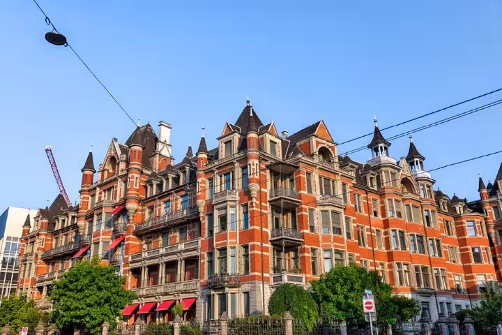 Victorian red brick mansion building with turrets and ornate facades on a sunny street in Zurich